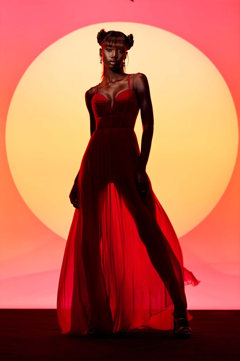 A full-body silhouette pictorial of a model in a red sheer dress against a large, circular orange sun-like backdrop.