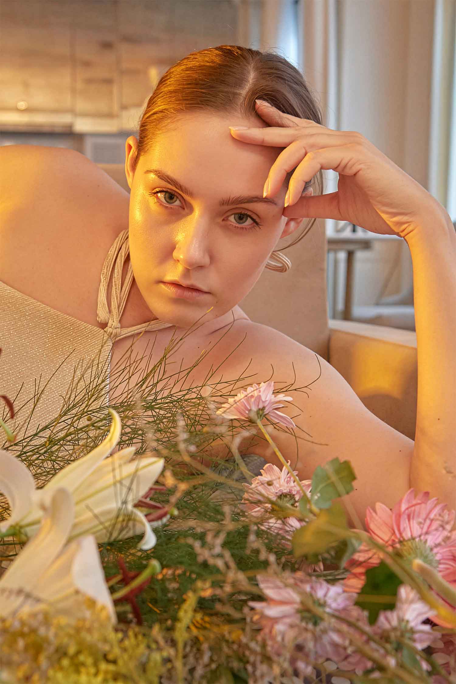 Portrait of a woman resting beside fresh flowers in warm natural window light. Natural light portrait of a woman with flowers indoors.